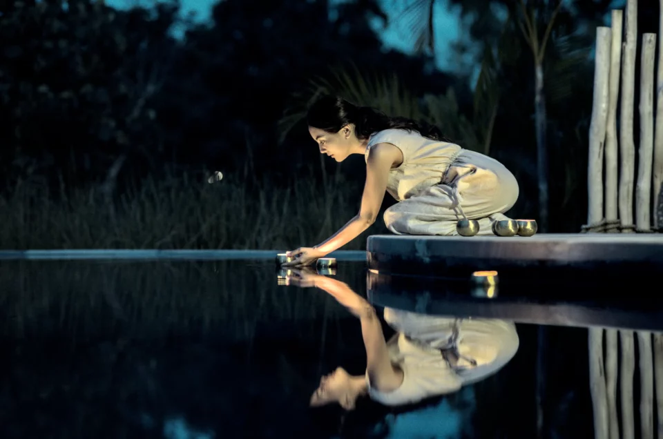 Girl places a candle in still water for Namia River Retreat