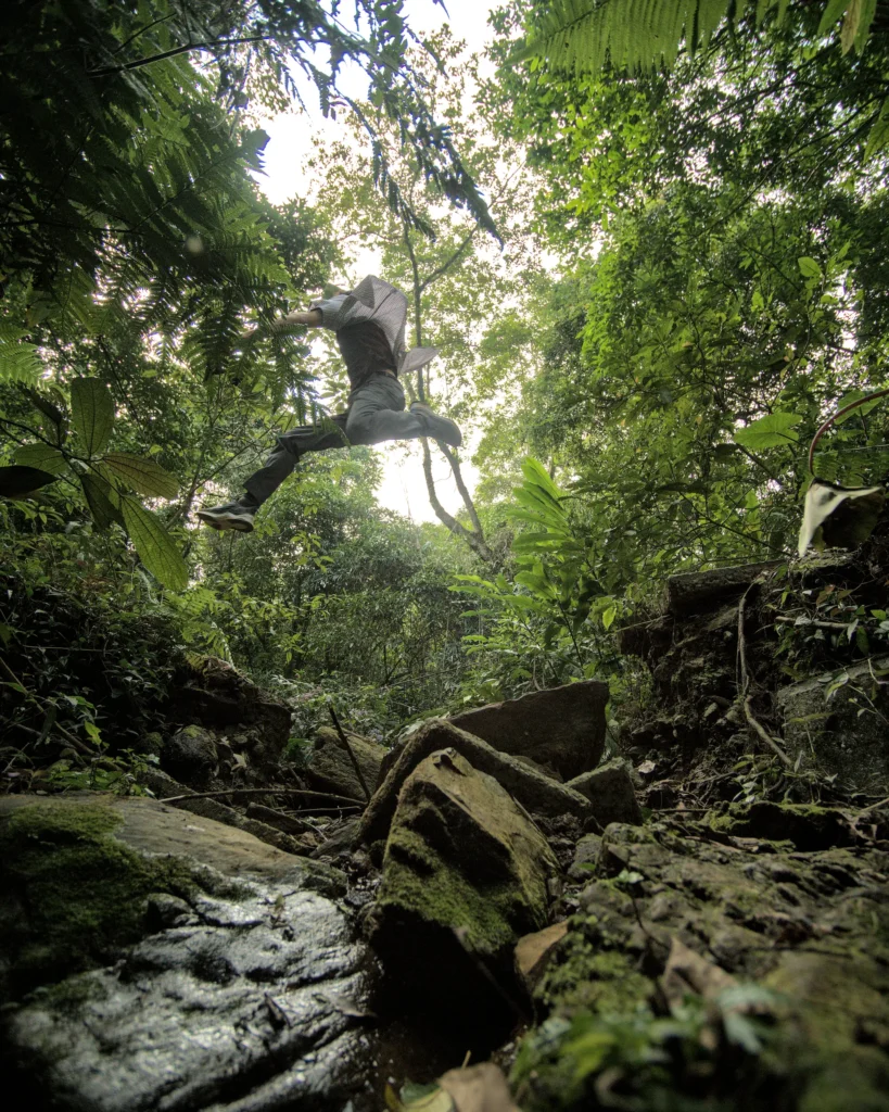 A man leaps over a large gap in the jungle.